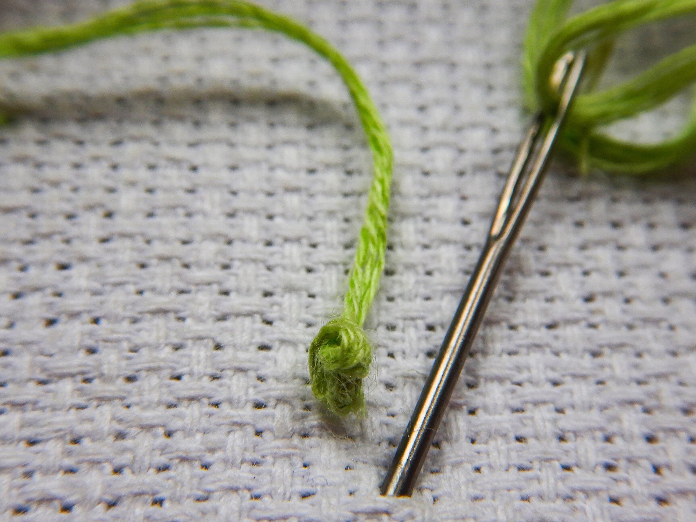 Agulha com linha verde sobre tecido de trama aberta